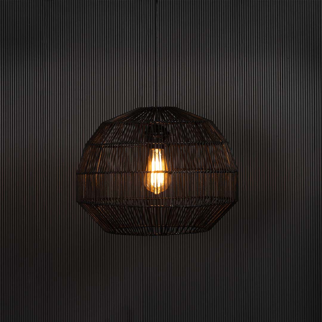 Stylish black pendant lamp illuminated on dark background casting warm soft light through intricate handwoven rattan design.