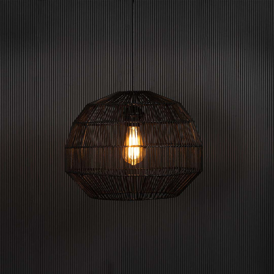 Stylish black pendant lamp illuminated on dark background casting warm soft light through intricate handwoven rattan design.