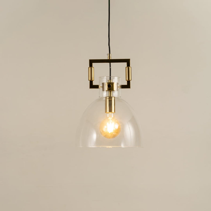 Clear dome glass pendant light with gold detailing shown with light on against a white background highlighting its warm glow and modern style.