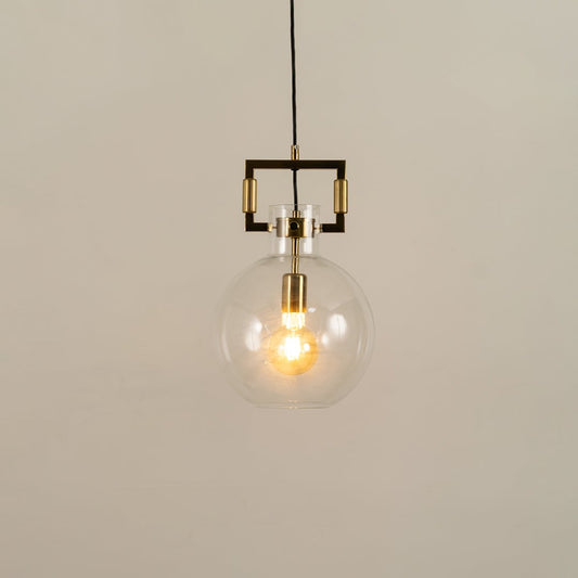 Clear glass globe pendant light with gold hardware shown with light on against a white background highlighting its warm glow and modern design.