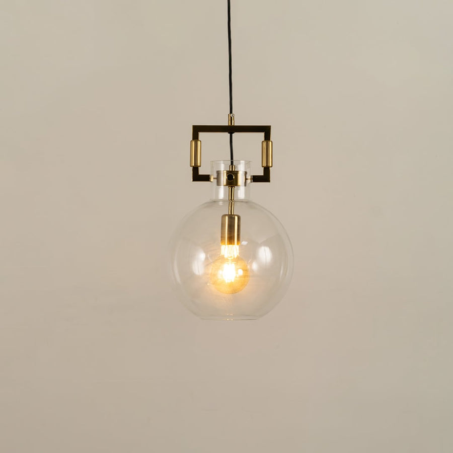 Clear glass globe pendant light with gold hardware shown with light on against a white background highlighting its warm glow and modern design.