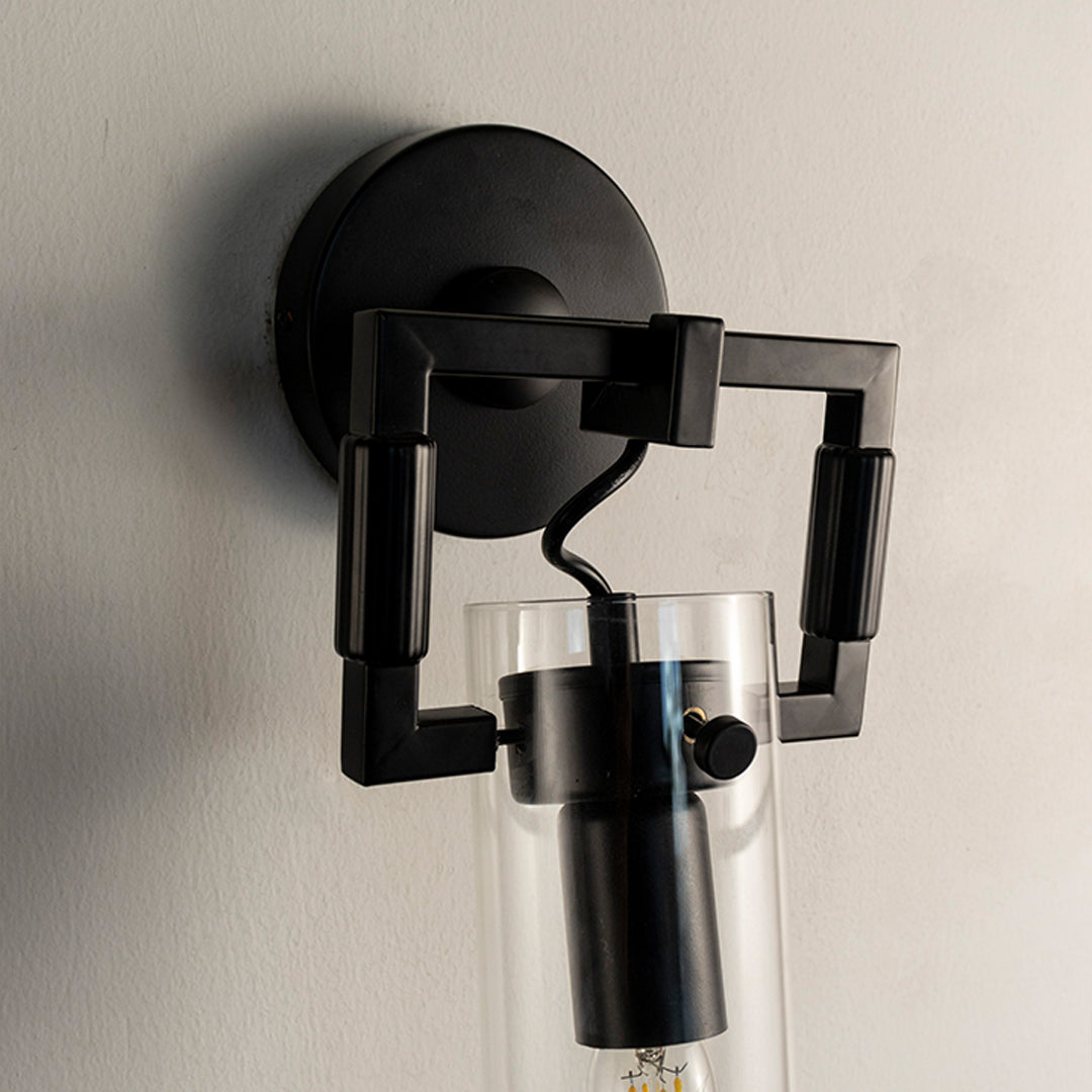 Closeup of modern black metal wall light with clear glass tube shade for luxury bedroom and hallway decor spaces.