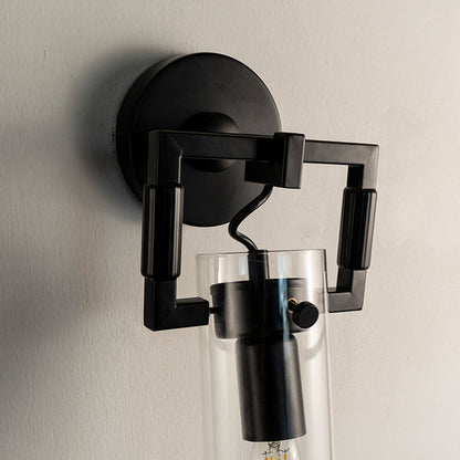 Closeup of modern black metal wall light with clear glass tube shade for luxury bedroom and hallway decor spaces.