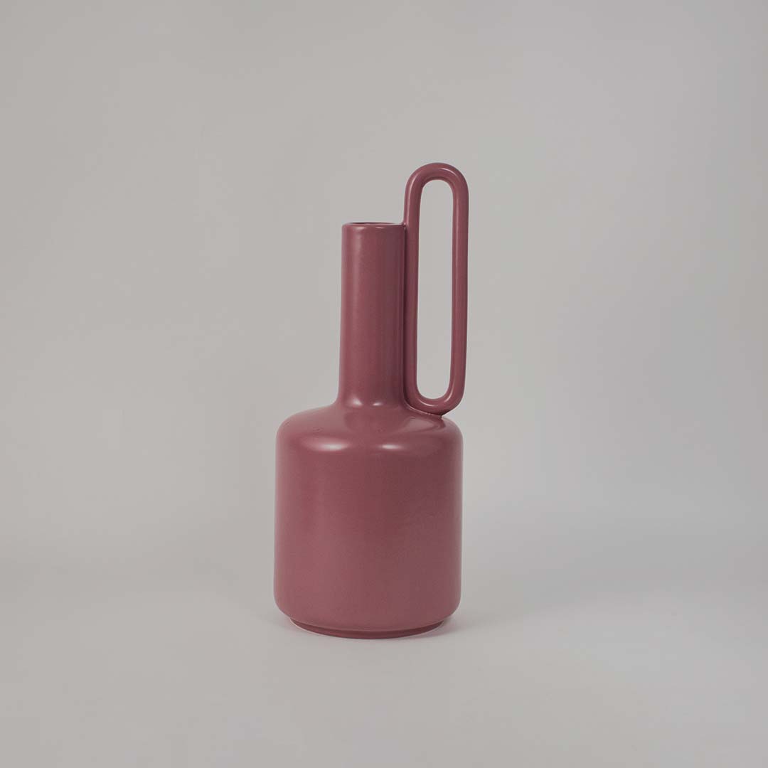 Elegant pink ceramic vase placed on a plain white background showcasing its glossy finish and tall artistic silhouette.