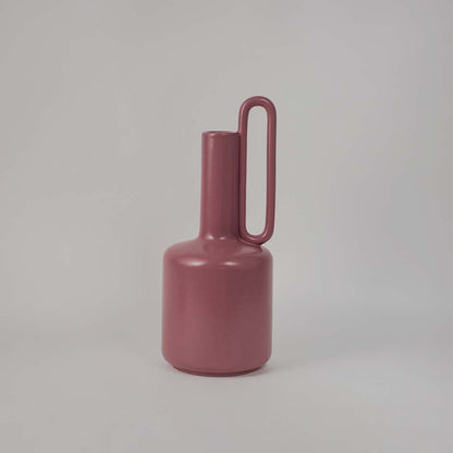 Elegant pink ceramic vase placed on a plain white background showcasing its glossy finish and tall artistic silhouette.