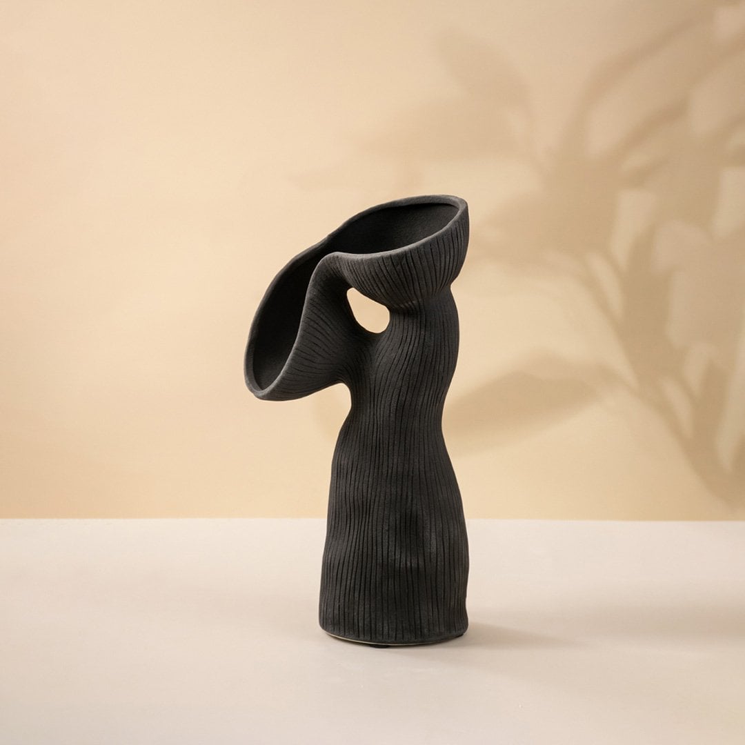 Contemporary black ceramic vase featuring unique flowing curves and ribbed surface texture on white surface.