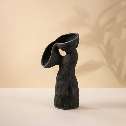 Contemporary black ceramic vase featuring unique flowing curves and ribbed surface texture on white surface.