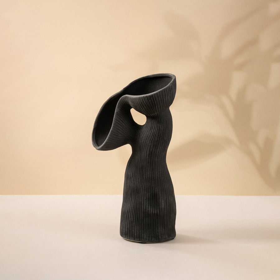 Contemporary black ceramic vase featuring unique flowing curves and ribbed surface texture on white surface.