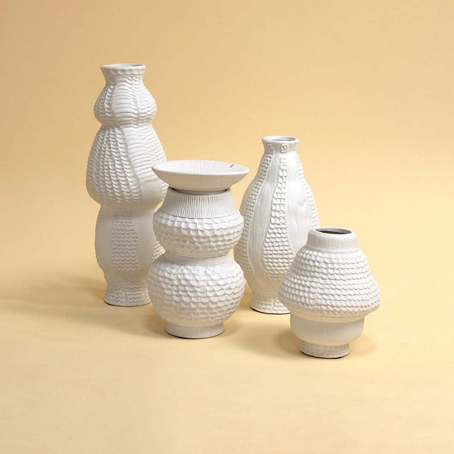Set of white textured ceramic vases with modern artistic shapes arranged together on white background creating a cohesive decor display.
