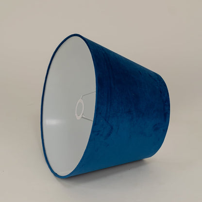 Modern blue velvet lampshade placed against a plain white background capturing its soft surface and contemporary tapered design.
