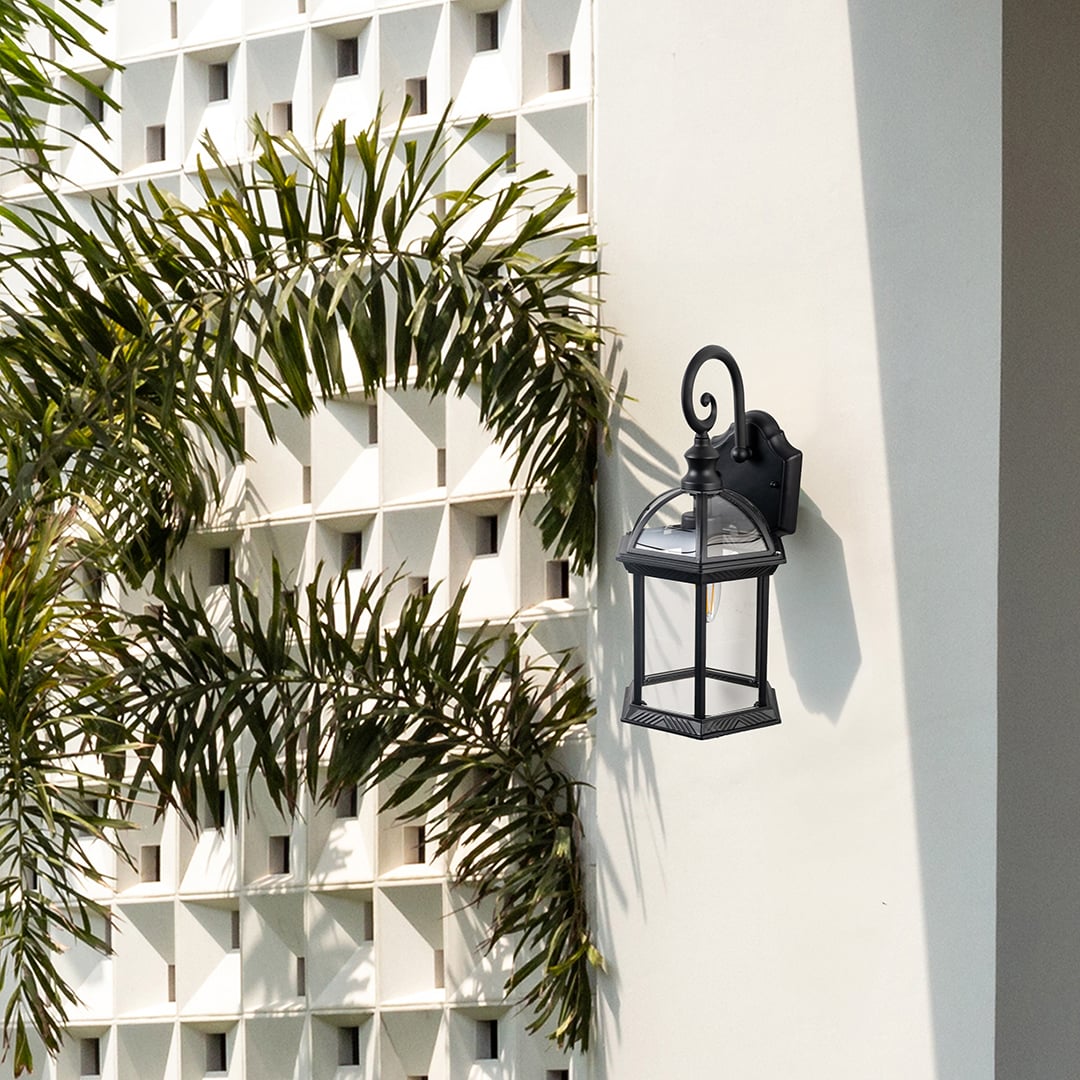 Black metal outdoor wall lantern installed on exterior wall near plants adding classic charm and functional lighting.