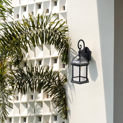 Black metal outdoor wall lantern installed on exterior wall near plants adding classic charm and functional lighting.
