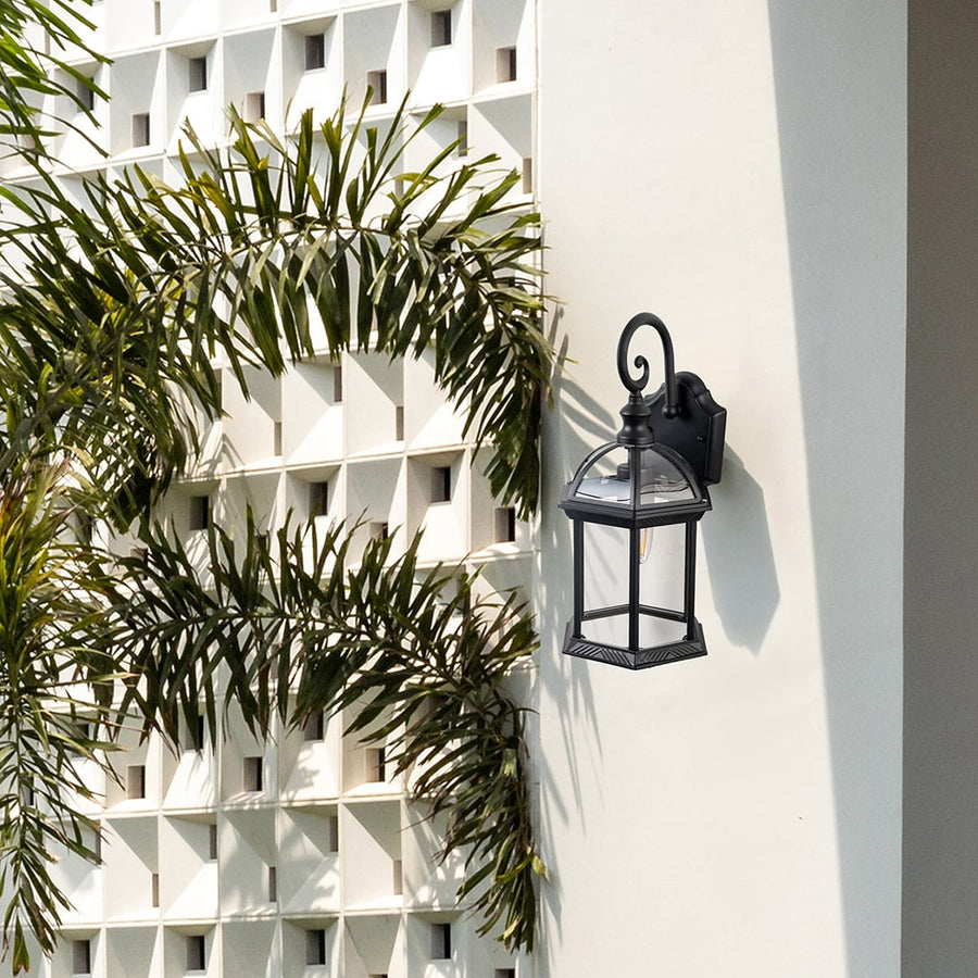 Black metal outdoor wall lantern installed on exterior wall near plants adding classic charm and functional lighting.