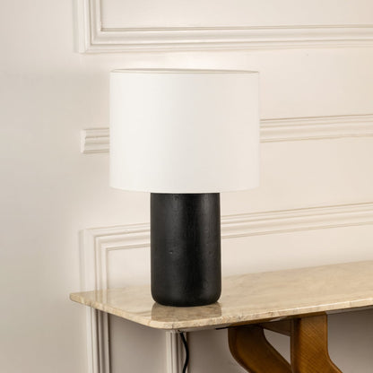 Black ceramic table lamp with cylindrical textured base and white fabric shade for modern interior decor styling.