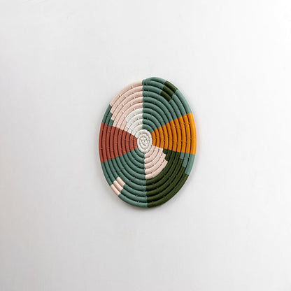 A handcrafted woven plate displayed from a subtle side angle against a plain white background emphasizing the raised spiral detailing.