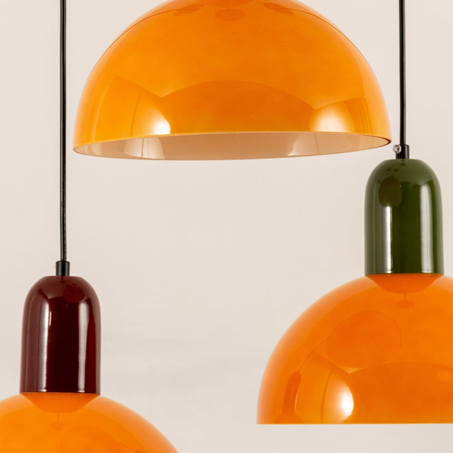 Hanging pendant lights in glossy orange shades with green and brown tops bring a bold and modern accent to interior spaces.