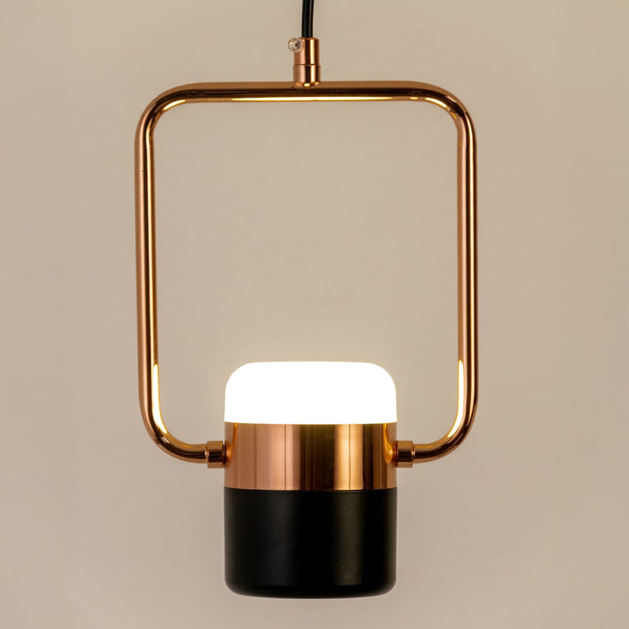 Closeup of rose gold pendant light showing sleek square frame and black and white diffuser for modern interior home decor.