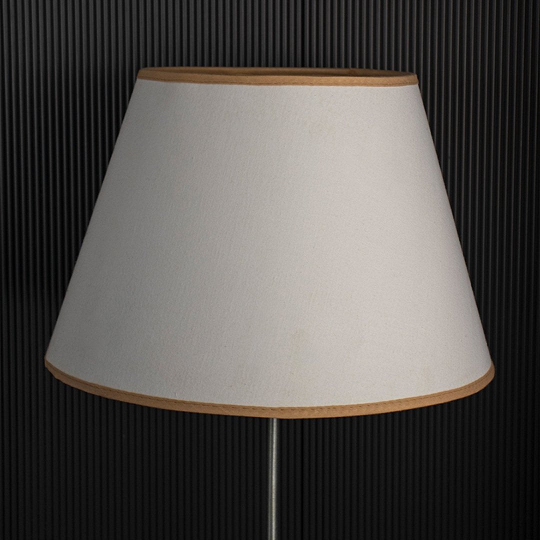 A classic tapered lampshade shown with light off black background highlighting its smooth beige fabric shape and clean stitched edges in a simple minimal style.