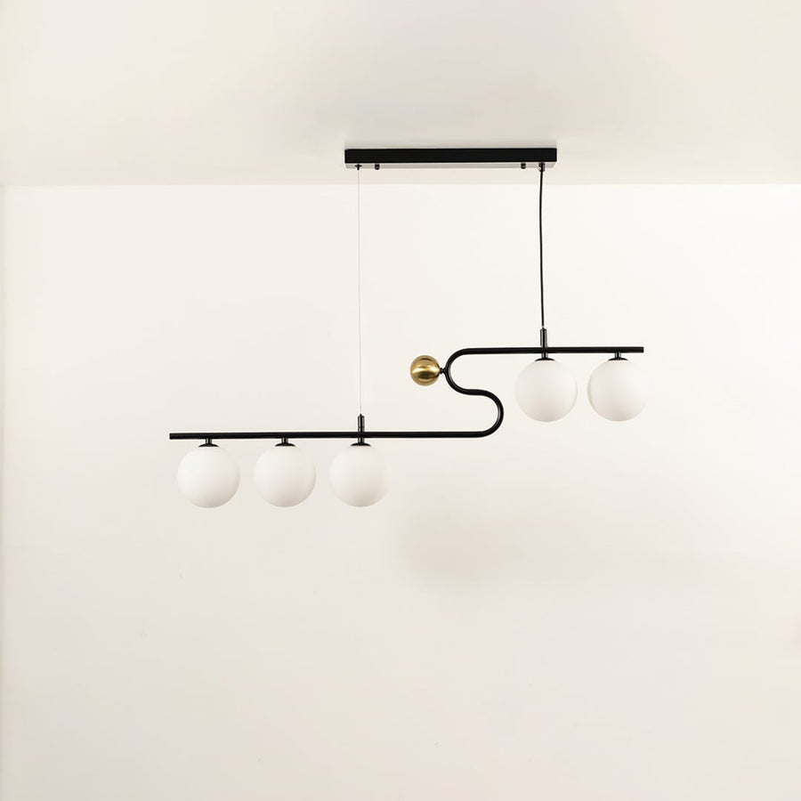 A sculptural black and gold linear chandelier with four glowing white globes suspended on a plain white background creating stylish warm lighting and refined décor.