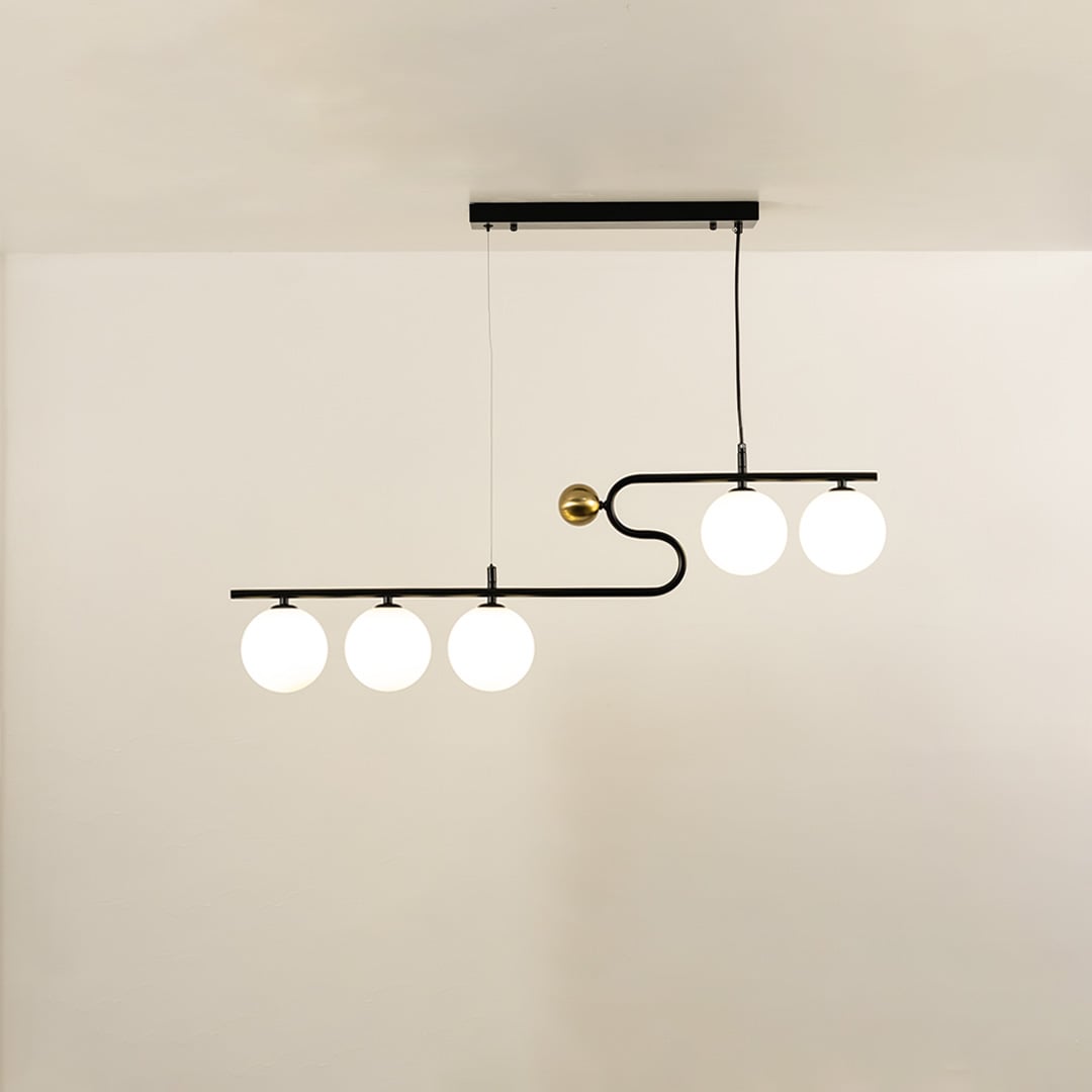 A sculptural black and gold linear chandelier with four glowing white globes hanging against a soft neutral background adding stylish warm lighting and artistic décor.
