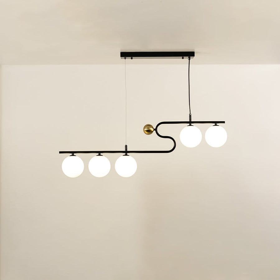 A sculptural black and gold linear chandelier with four glowing white globes hanging against a soft neutral background adding stylish warm lighting and artistic décor.