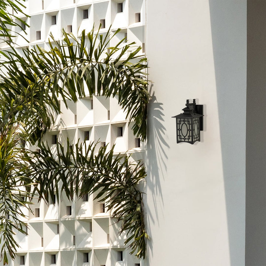 Black metal outdoor wall lantern with decorative oval pattern and frosted glass displayed on a white exterior wall adding elegant architectural outdoor styling.