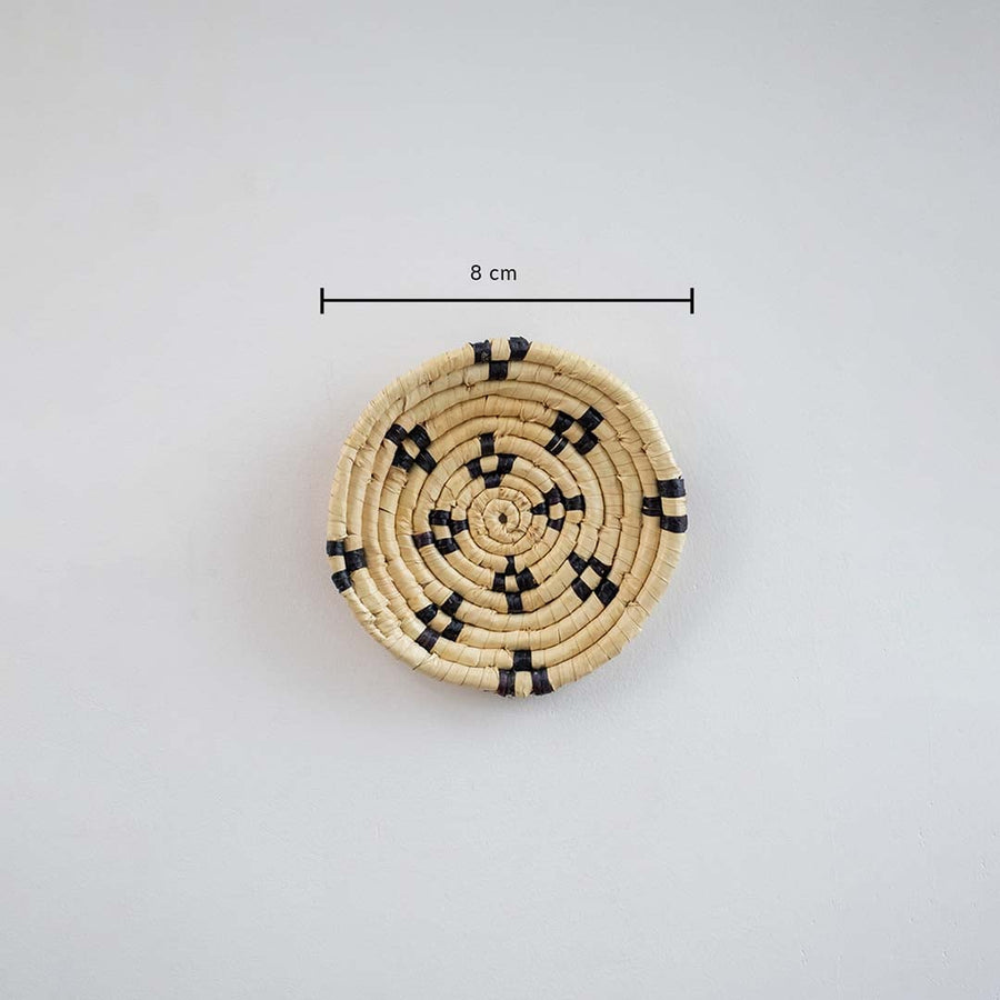 Handwoven round wall basket in natural and black tones showing approx 25 cm diameter for decorative wall placement reference.