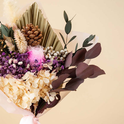 Closeup of a rustic dried flower bouquet with purple filler flowers brown eucalyptus leaves and a natural pinecone stem.