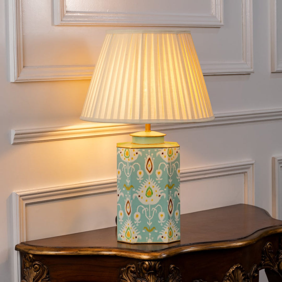 Stylish table lamp with pleated white shade and light blue ceramic base showcasing symmetrical motifs and refined gold detailing.