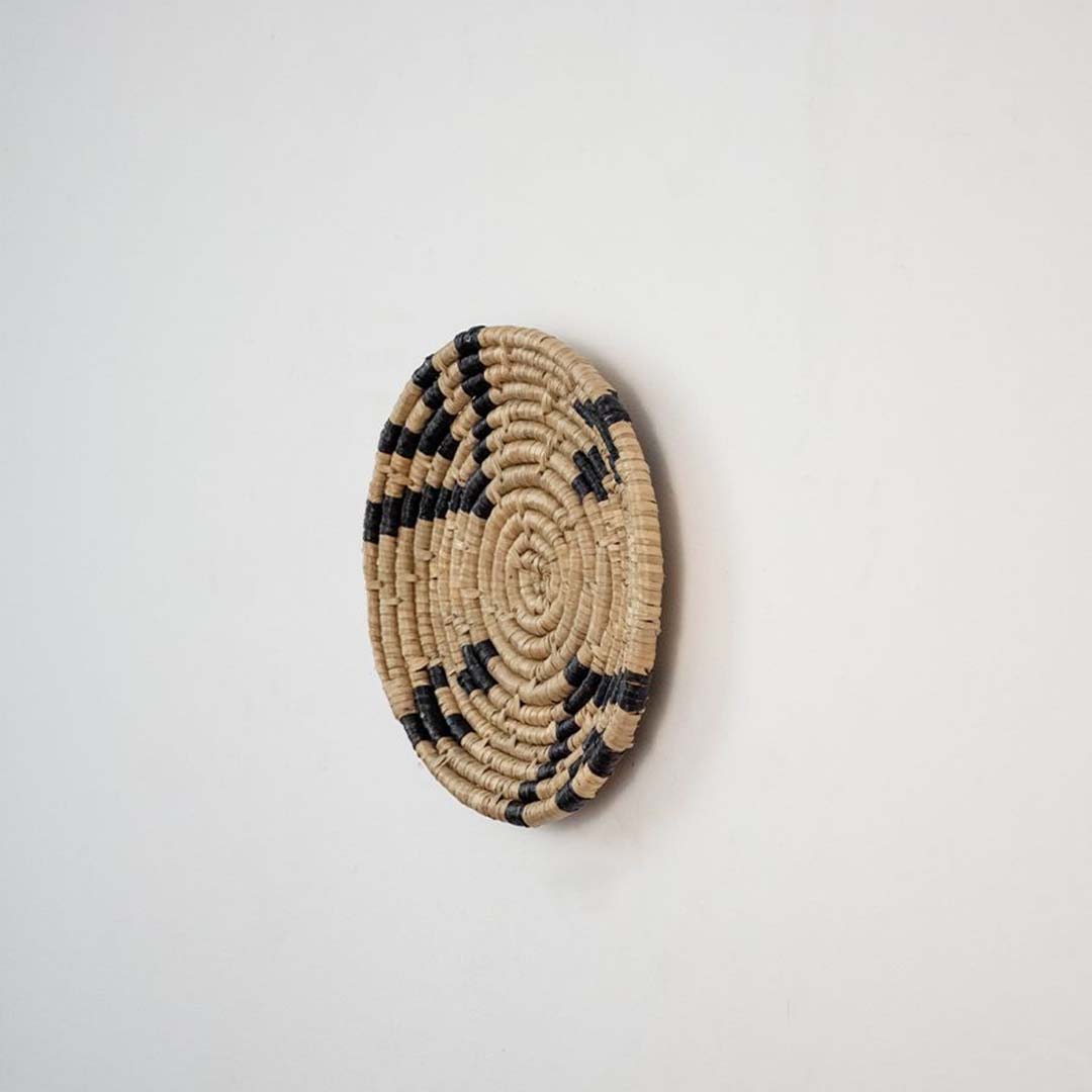 Decorative wicker wall decor basket in round shape with black and beige weaving for rustic wall styling.