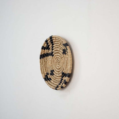 Decorative wicker wall decor basket in round shape with black and beige weaving for rustic wall styling.