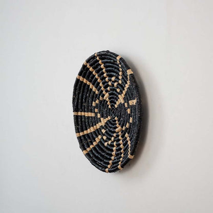 Side view of a black and beige woven basket with intricate spiral design highlighting the texture and craftsmanship.