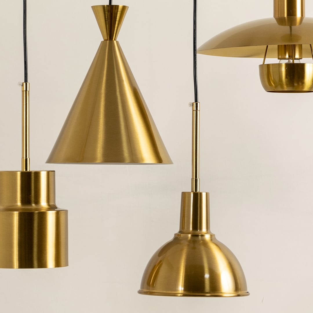 A group of metal pendant lights glowing softly against a plain light background featuring cone dome and tiered shapes adding refined modern metallic décor.