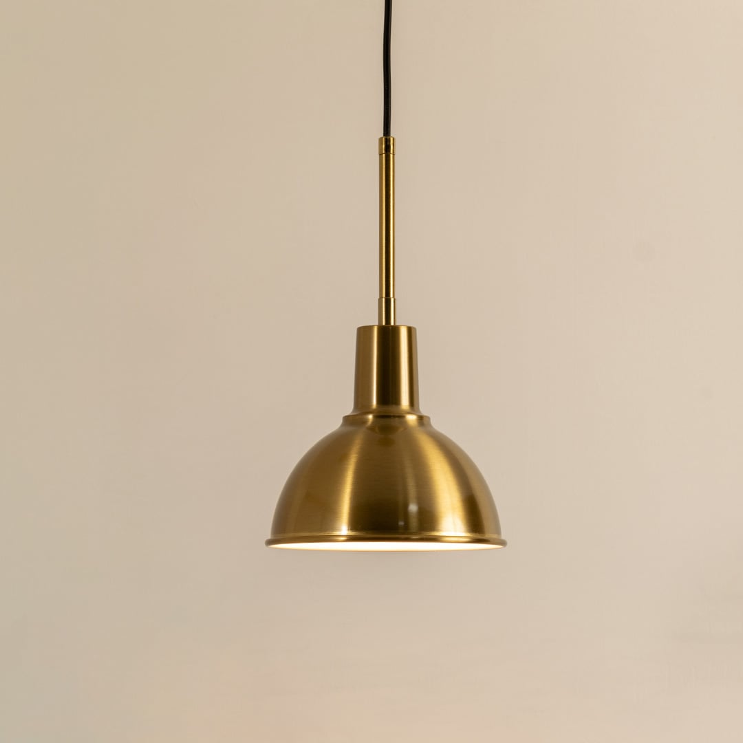 A metal dome pendant light glowing warmly against a neutral beige backdrop offering classic soft illumination and timeless modern interior décor.