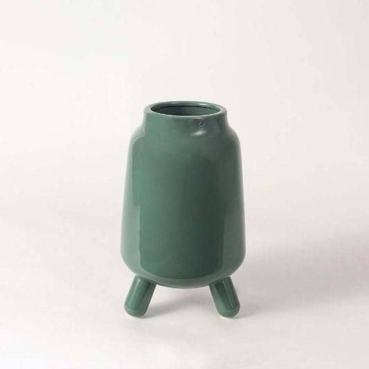 A modern green ceramic vase with tripod legs displayed on a clean white background showing its smooth glossy finish and contemporary shape.