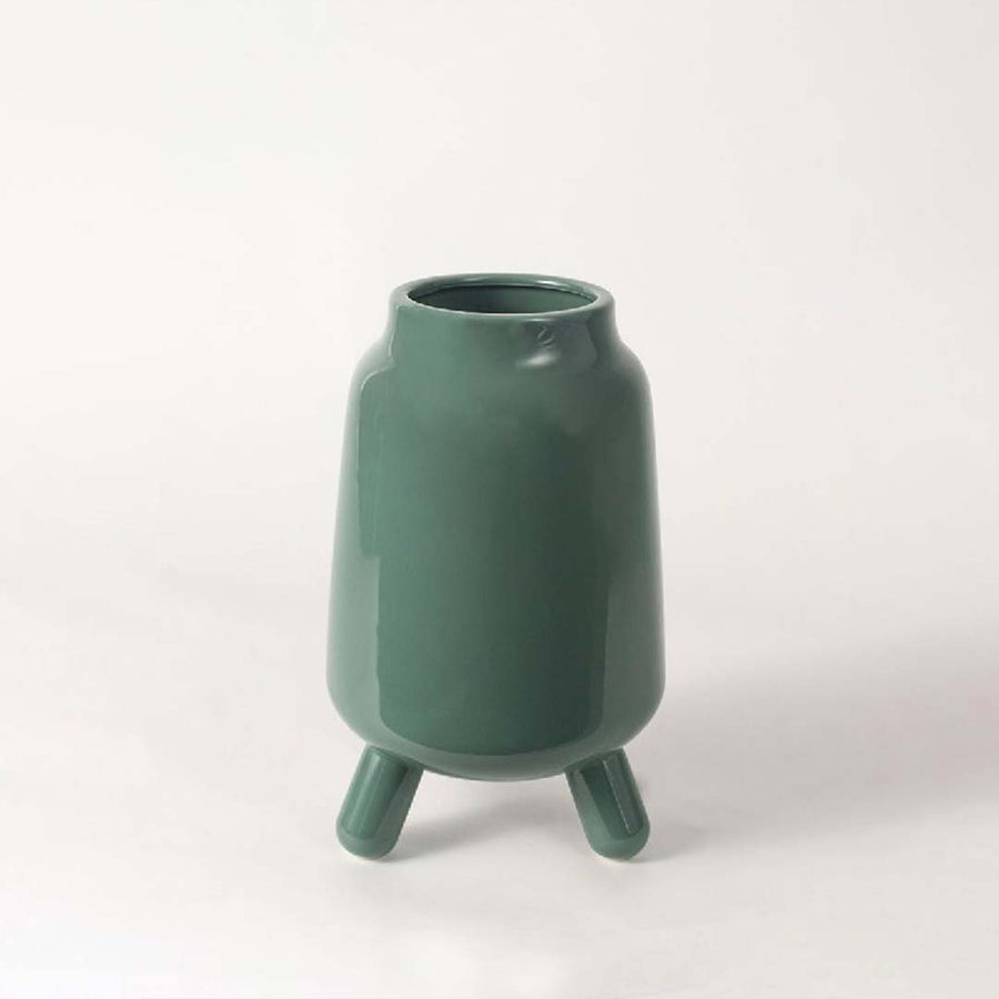 A modern green ceramic vase with tripod legs displayed on a clean white background showing its smooth glossy finish and contemporary shape.