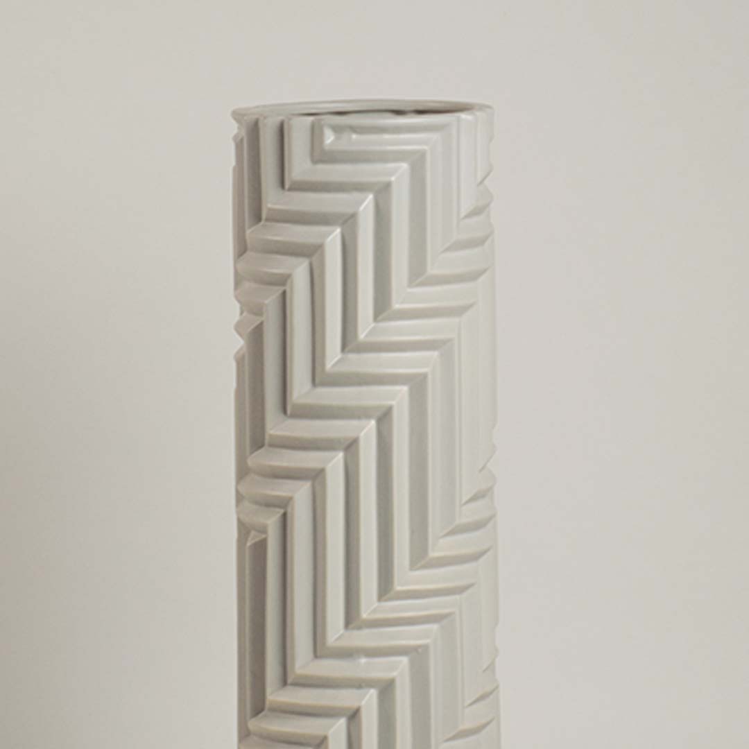 Minimal white ceramic vase with raised zigzag patterns captured in soft ambient light emphasizing its sculptural details.