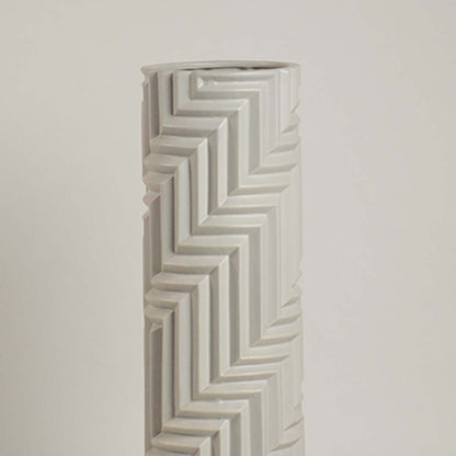 Minimal white ceramic vase with raised zigzag patterns captured in soft ambient light emphasizing its sculptural details.