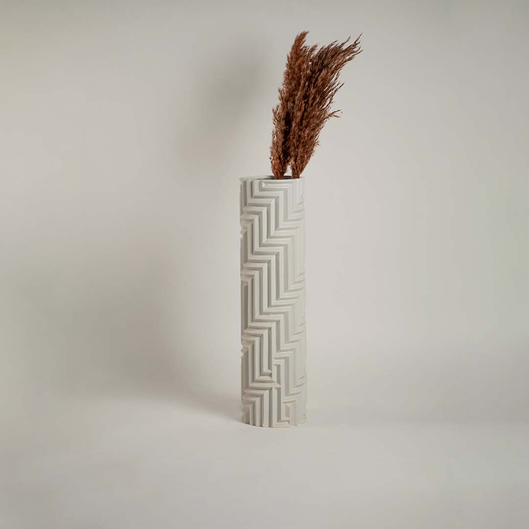White ceramic vase with geometric detailing against a clean white backdrop emphasizing its refined craftsmanship.