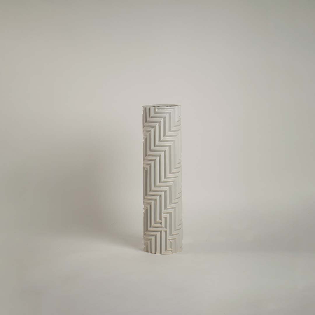 White geometric ceramic vase with angular embossed design highlighted under warm light against a white background for contrast.