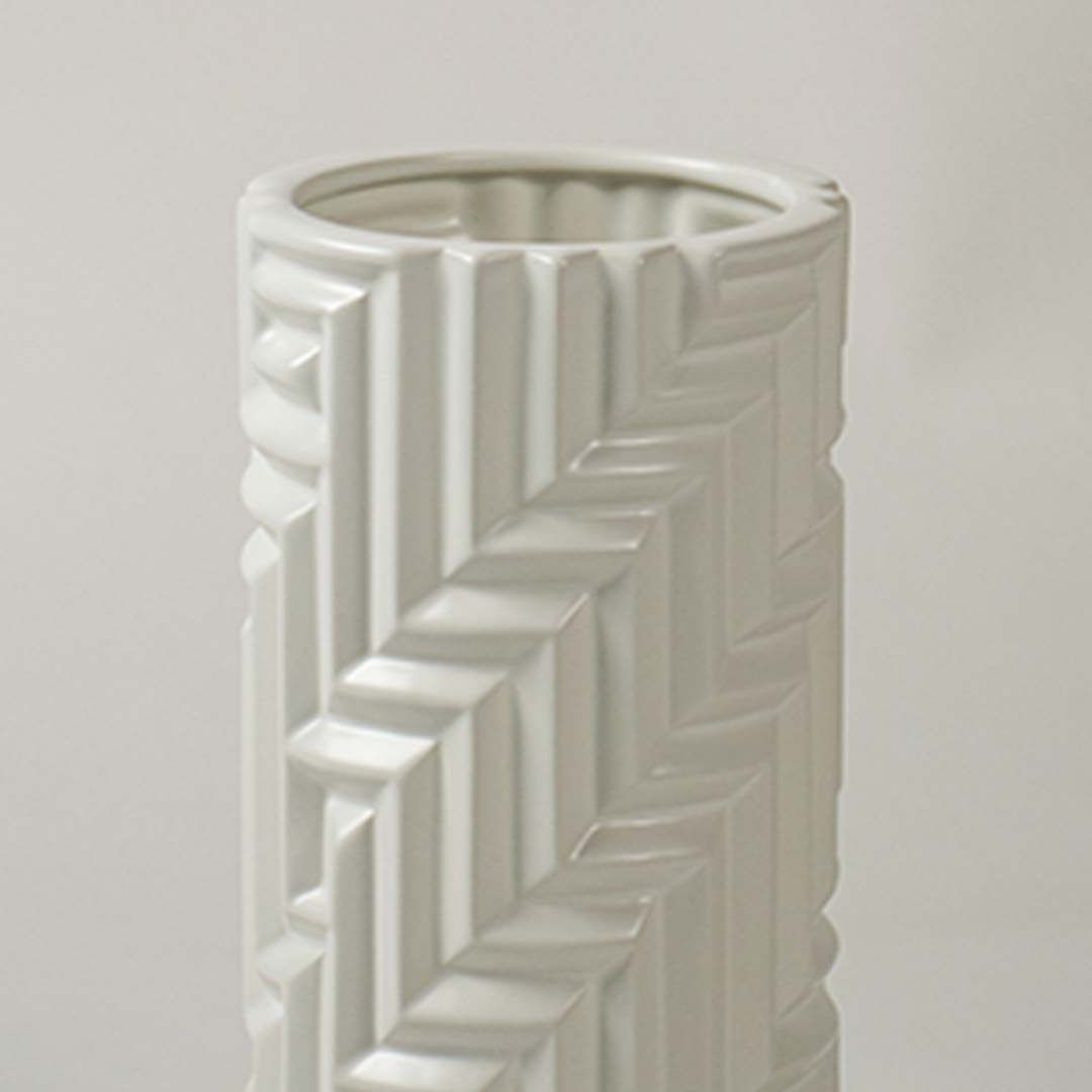 A detailed closeup of the white textured vase showing its raised geometric pattern and smooth cylindrical shape in a soft light background.