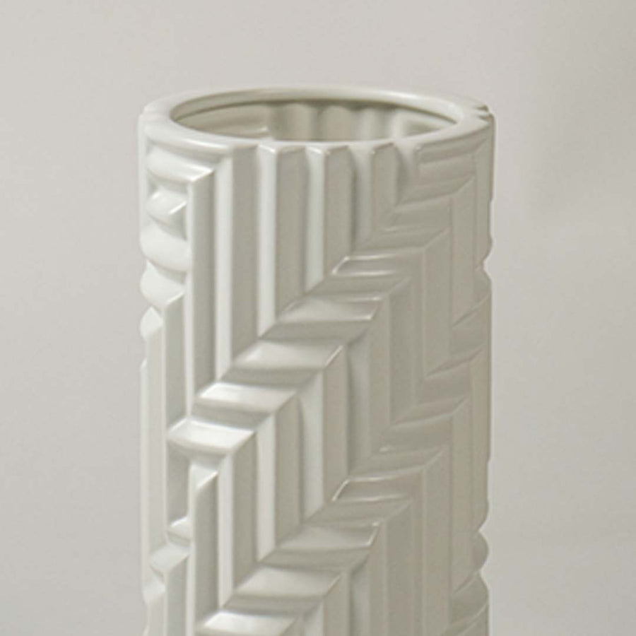 A detailed closeup of the white textured vase showing its raised geometric pattern and smooth cylindrical shape in a soft light background.