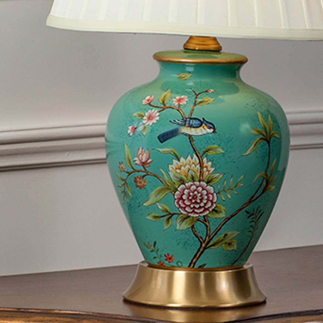 Closeup of green ceramic table lamp with floral hand-painted base golden accents and pleated fabric lampshade.