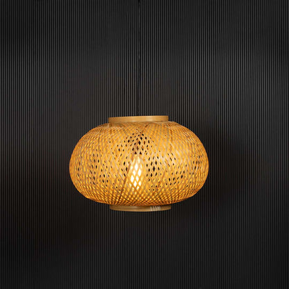 Round rattan pendant light with woven bamboo shade turned on glowing warmly against black background.