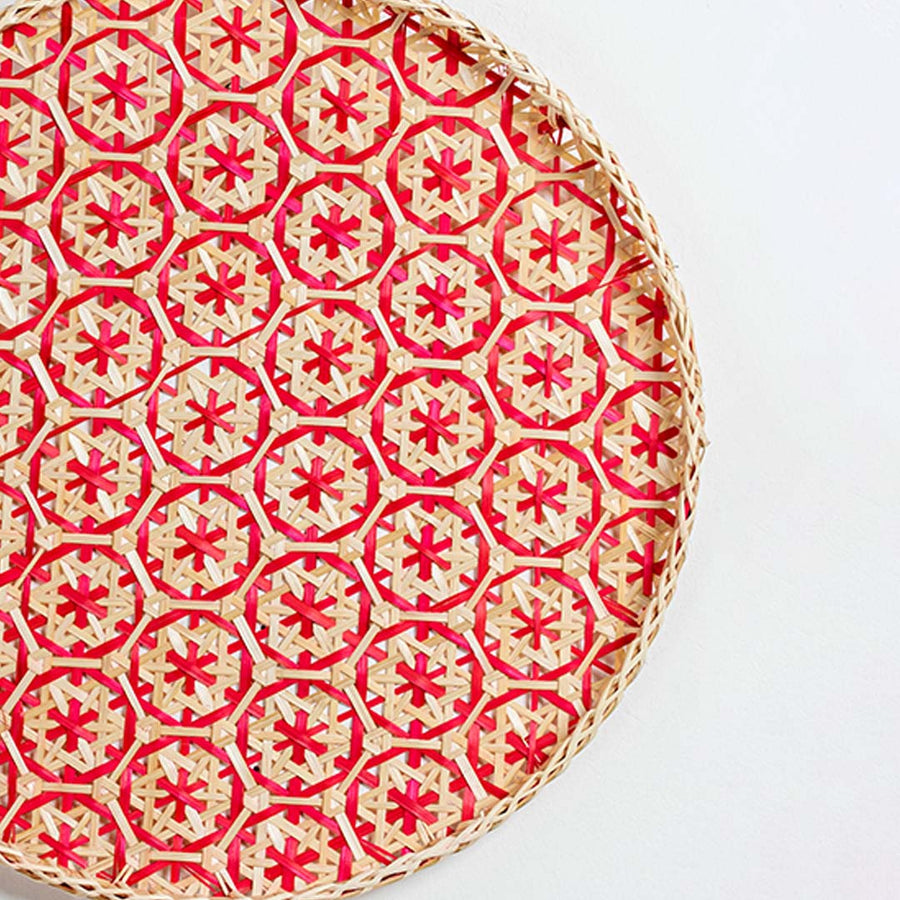 Closeup of handwoven bamboo basket showing intricate red geometric floral weave pattern and traditional artisan craftsmanship.