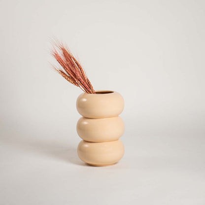 A beige sculptural ceramic vase placed on a wooden surface within a softly lit living space highlighting its smooth rounded form and adding a minimal contemporary decor touch.