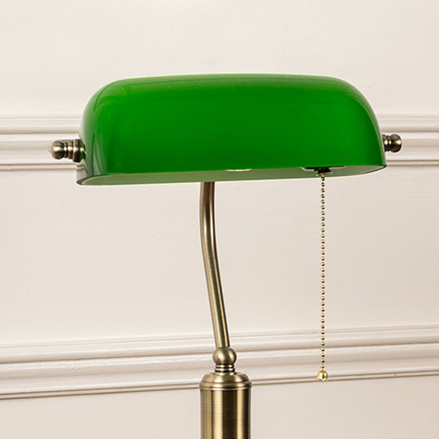 Closeup of green glass banker lamp highlighting antique brass base and pull chain switch for timeless decor charm.