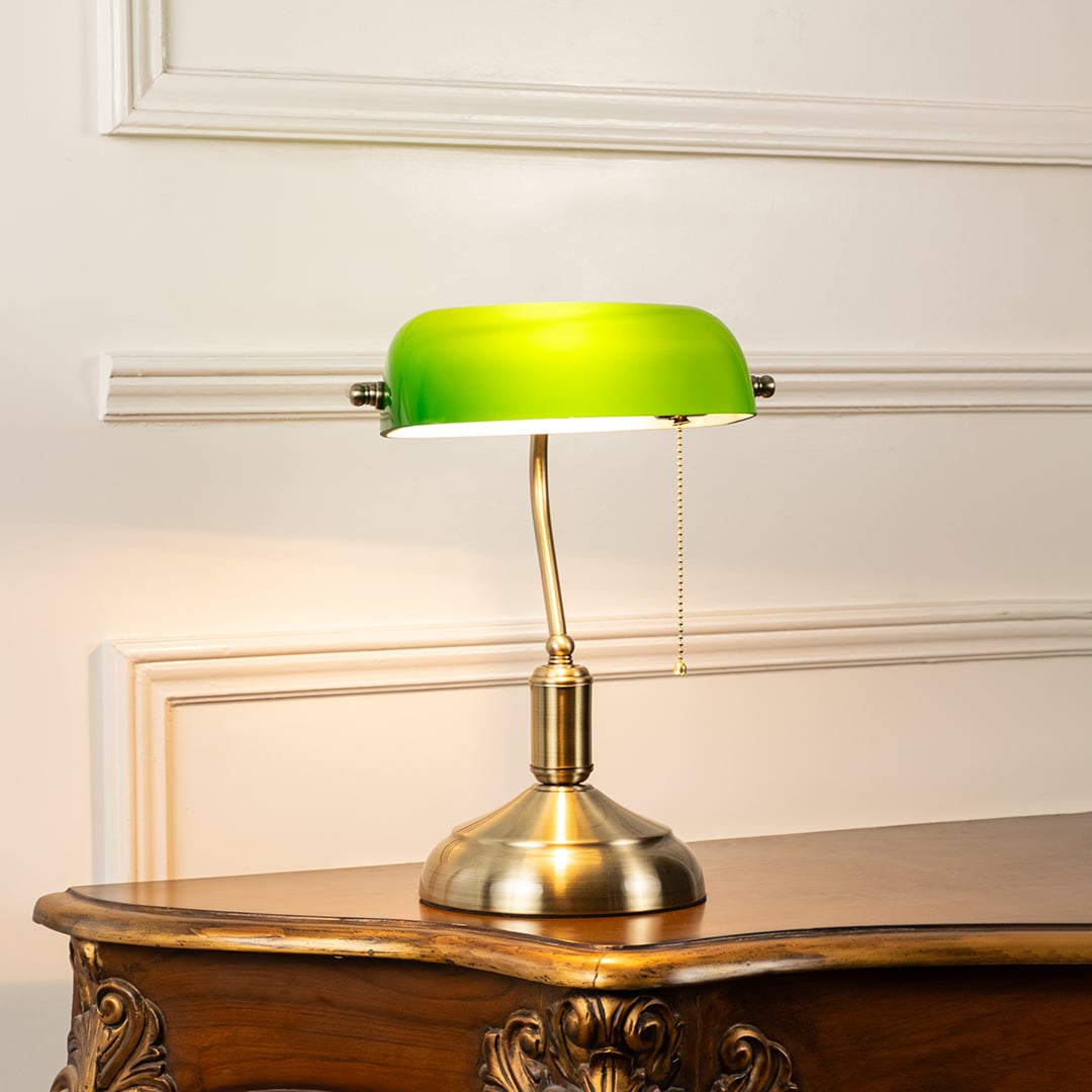 Elegant green glass and brass banker table lamp glowing warmly on white background for sophisticated interiors.