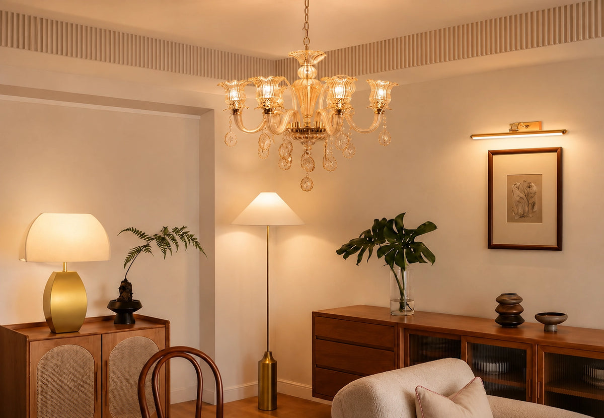 An elegant multi-light crystal chandelier hangs in a warm, modern living room setting with beige walls, a wooden console table, and other ambient lighting.