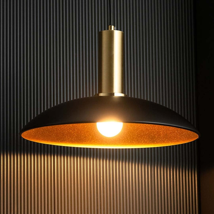 Closeup of black metal pendant light with warm glowing bulb gold inner reflector and sleek modern ceiling light design.
